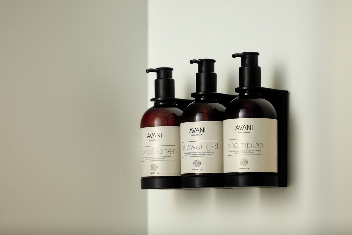 Trois bouteilles de produits AVANI sont posées sur une étagère noire, devant un mur blanc.
