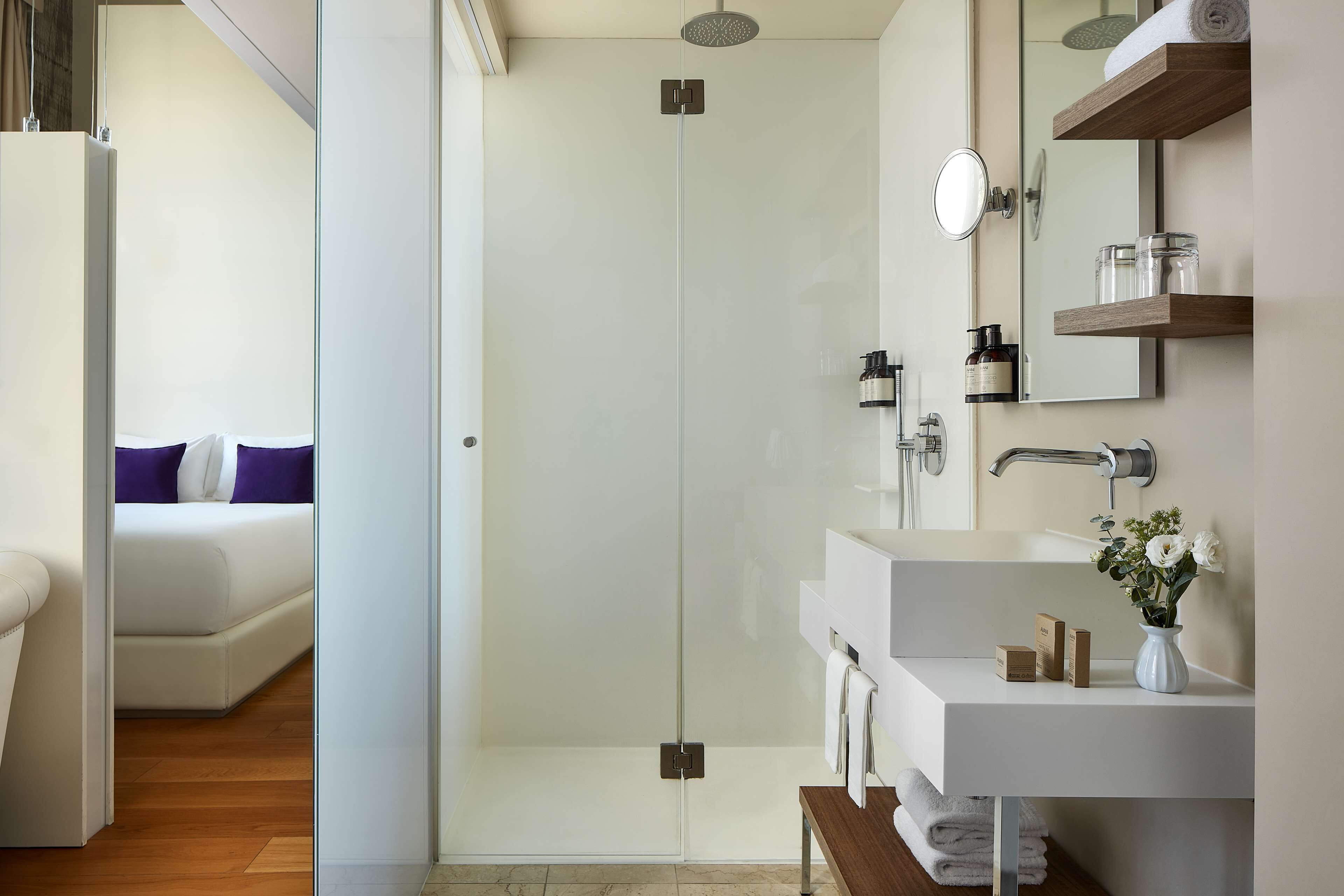A modern bathroom with a glass shower enclosure, a white sink with a mirror, and a wooden vanity.