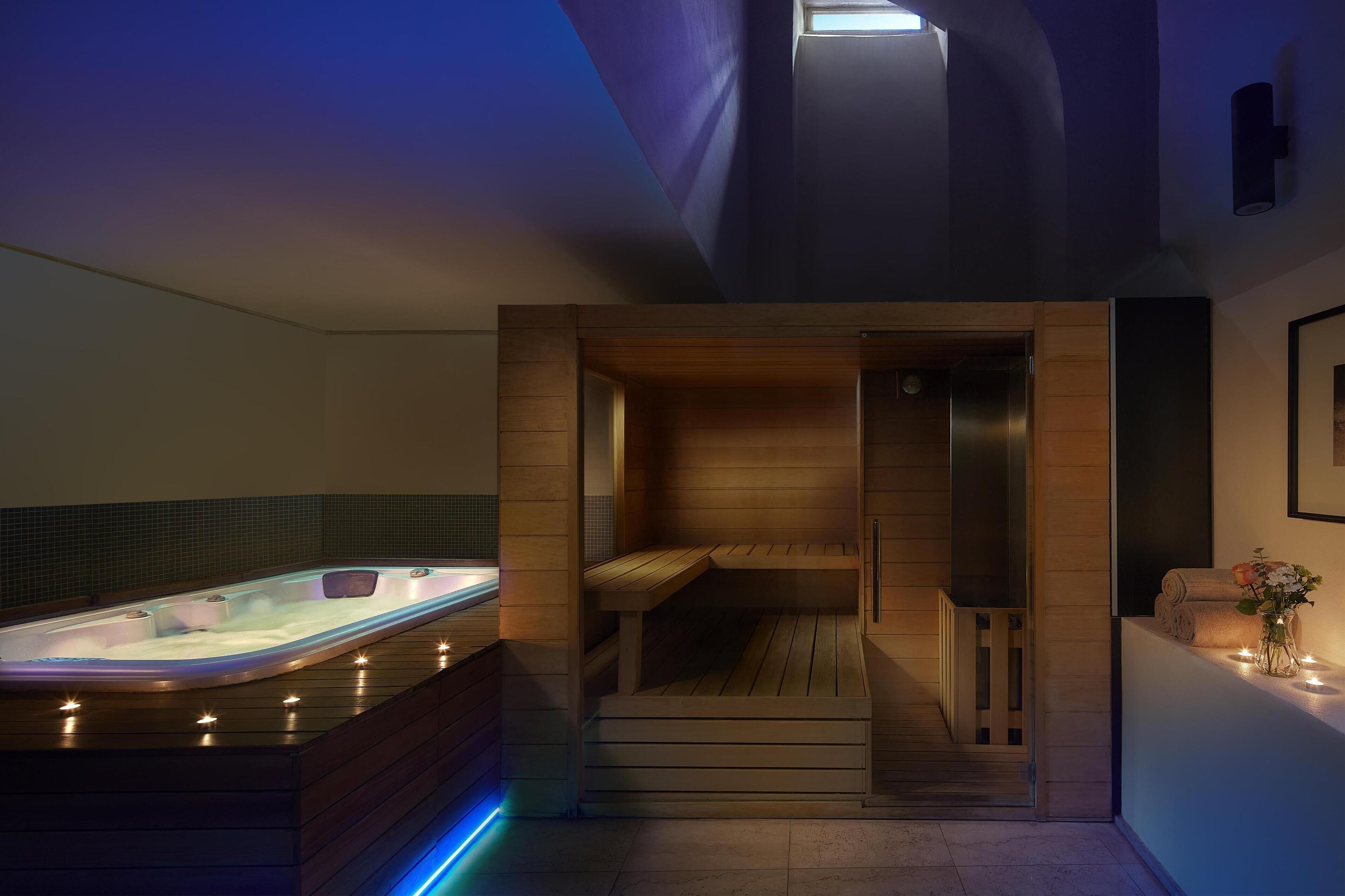 A modern spa room with a hot tub, wooden benches, and a small seating area.
