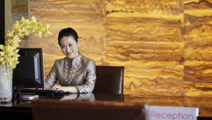 A reception desk with a marble wall background, a computer, and a vase with flowers. - Lake View Hotel (Beijing)