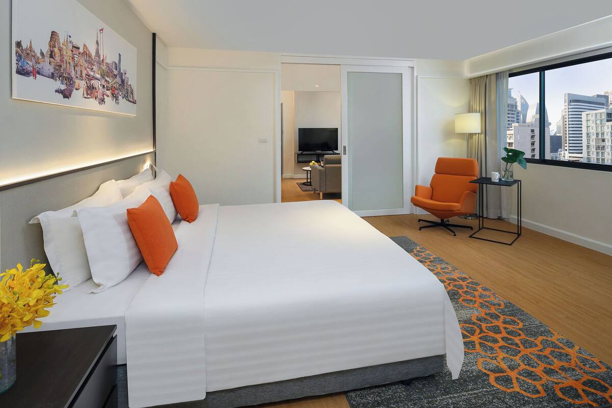 Habitación de hotel con una cama grande, un escritorio, una silla, un televisor y vistas a la ciudad.