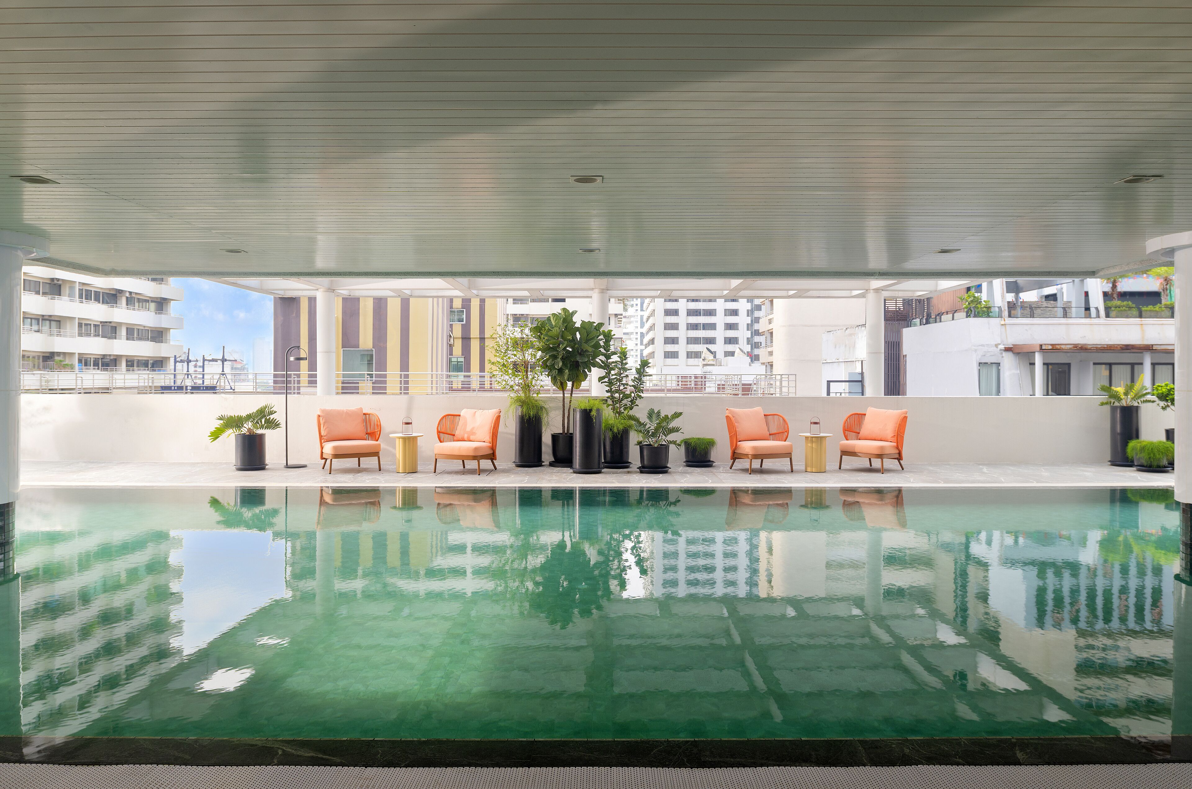 A rooftop pool with a clear view of the cityscape, surrounded by orange chairs and potted plants.