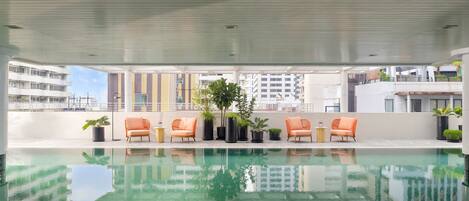 A rooftop pool with a clear view of the cityscape, surrounded by orange chairs and potted plants.