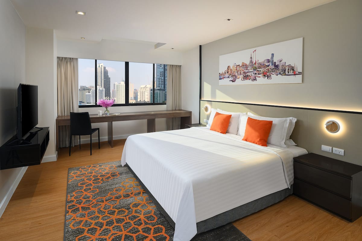 Habitación de hotel moderna con una cama grande, un escritorio con silla, televisión y vistas a la ciudad.