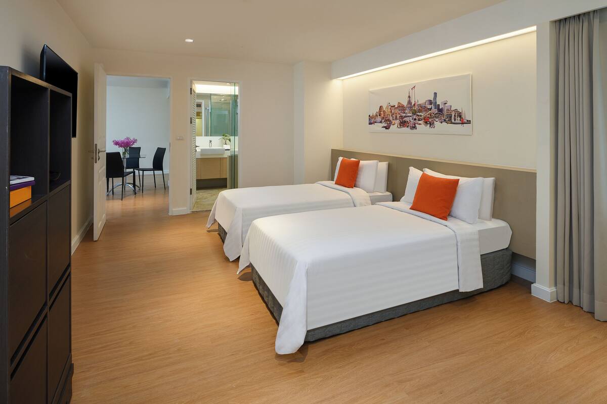 Habitación de hotel con dos camas, televisor y zona de comedor con sillas y mesa.