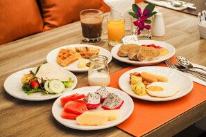 Uma mesa de café da manhã com pratos de comida, um copo de suco de laranja, um copo de café e um pequeno pote de leite.