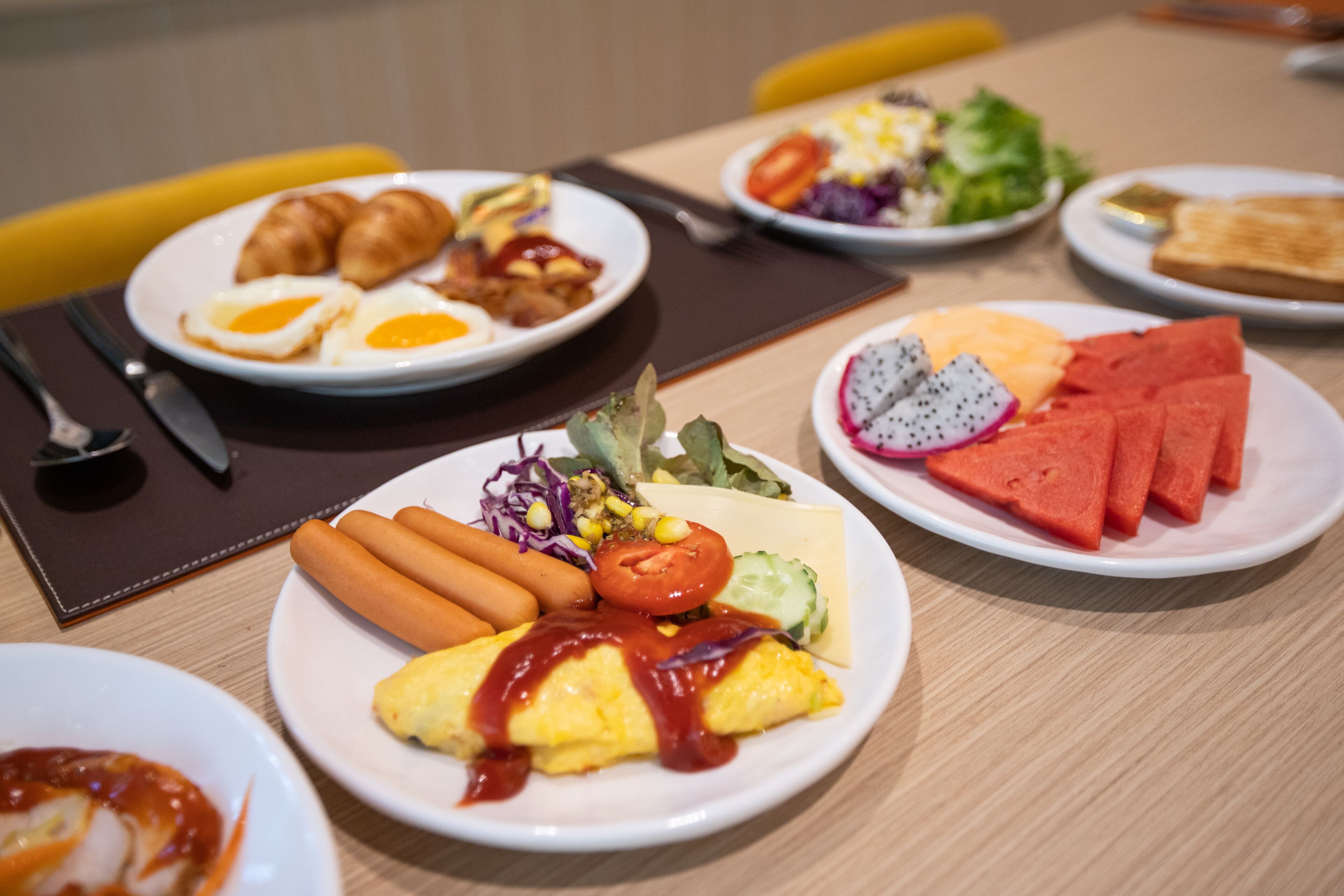 Un bufé de desayuno con diversos platos, como huevos, salchichas y rebanadas de sandía.