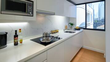 Een moderne keuken met een magnetron, fornuis en een spoelbak. Op het aanrecht staat een fles drank en een plant.