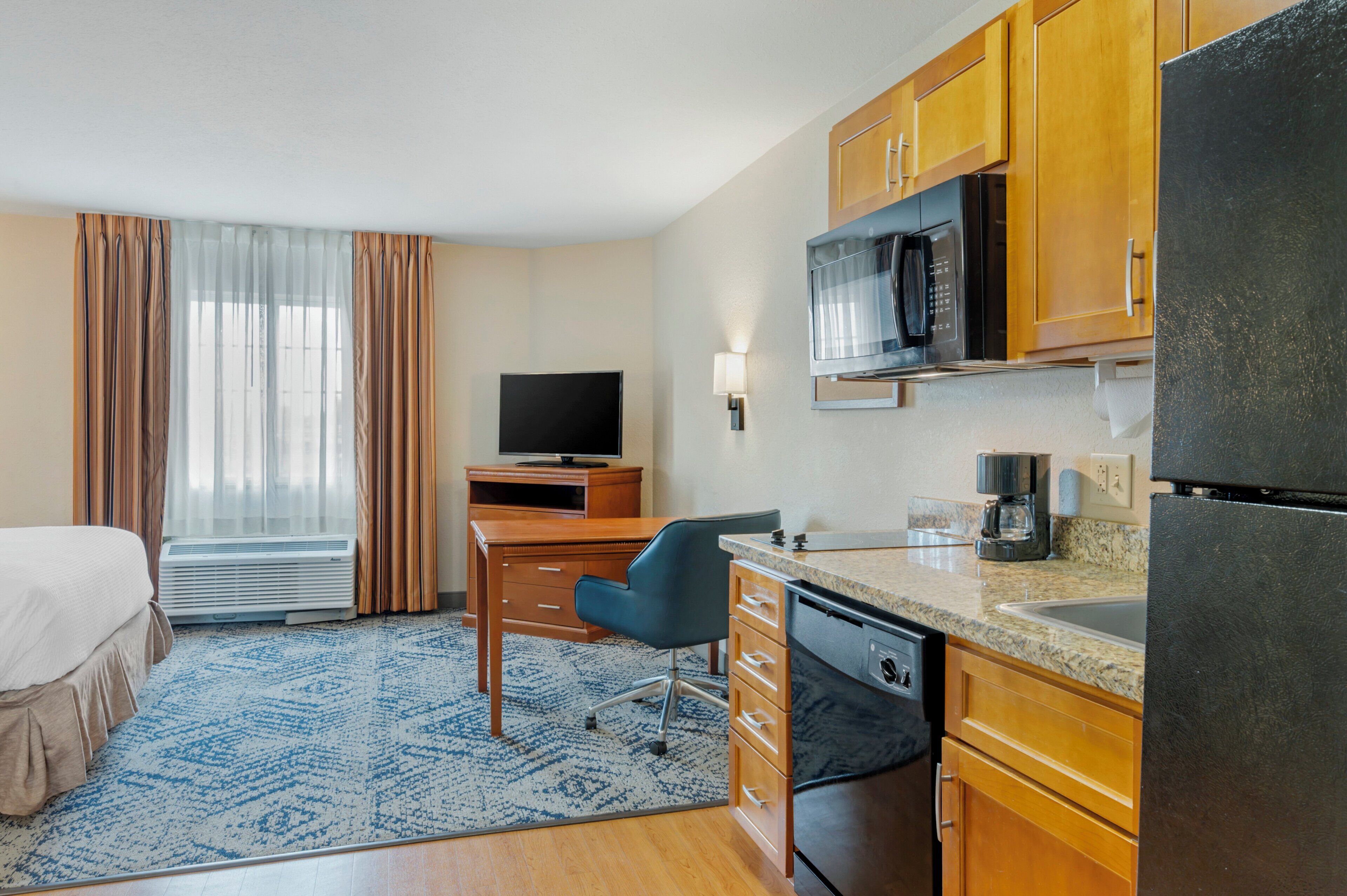 A hotel room with a bed, a desk, a television, a microwave, a refrigerator, and a coffee maker.