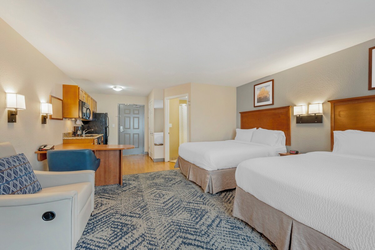 Habitación de hotel con dos camas, un escritorio, una silla y la puerta del baño.