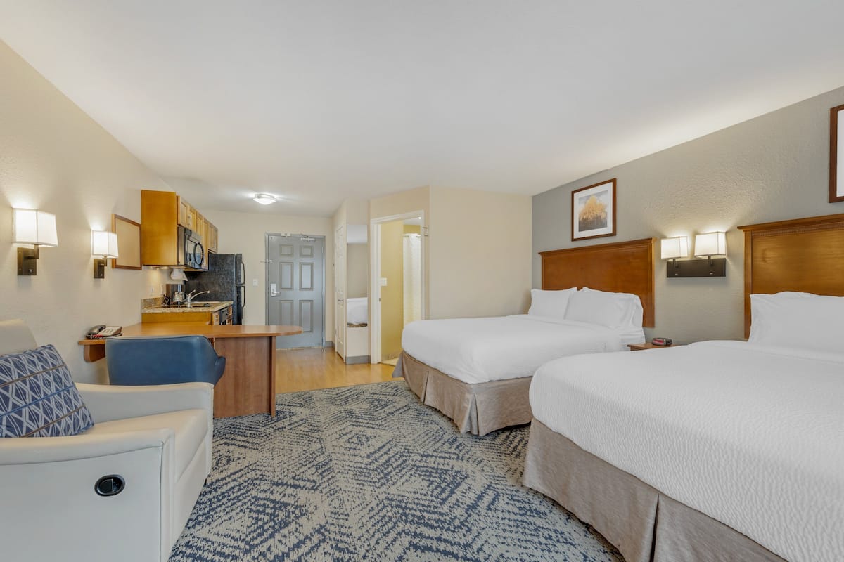 A hotel room with two beds, a desk, a chair, and a bathroom door.