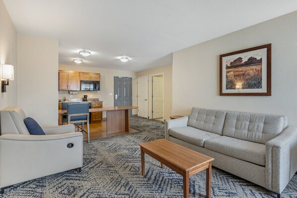 A modern living room with a sofa, a coffee table, and a dining area with a kitchen in the background.