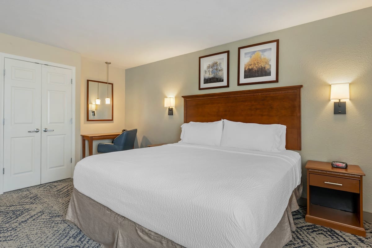 A hotel room with a large bed, a desk with a chair, a nightstand, and two wall-mounted lamps.