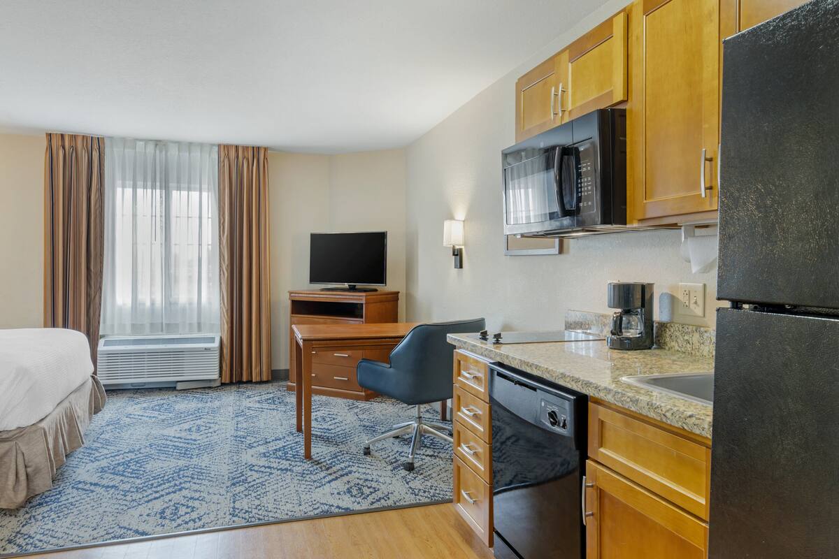 A hotel room with a bed, a desk with a chair, a television, a microwave, a refrigerator, and a window with curtains.