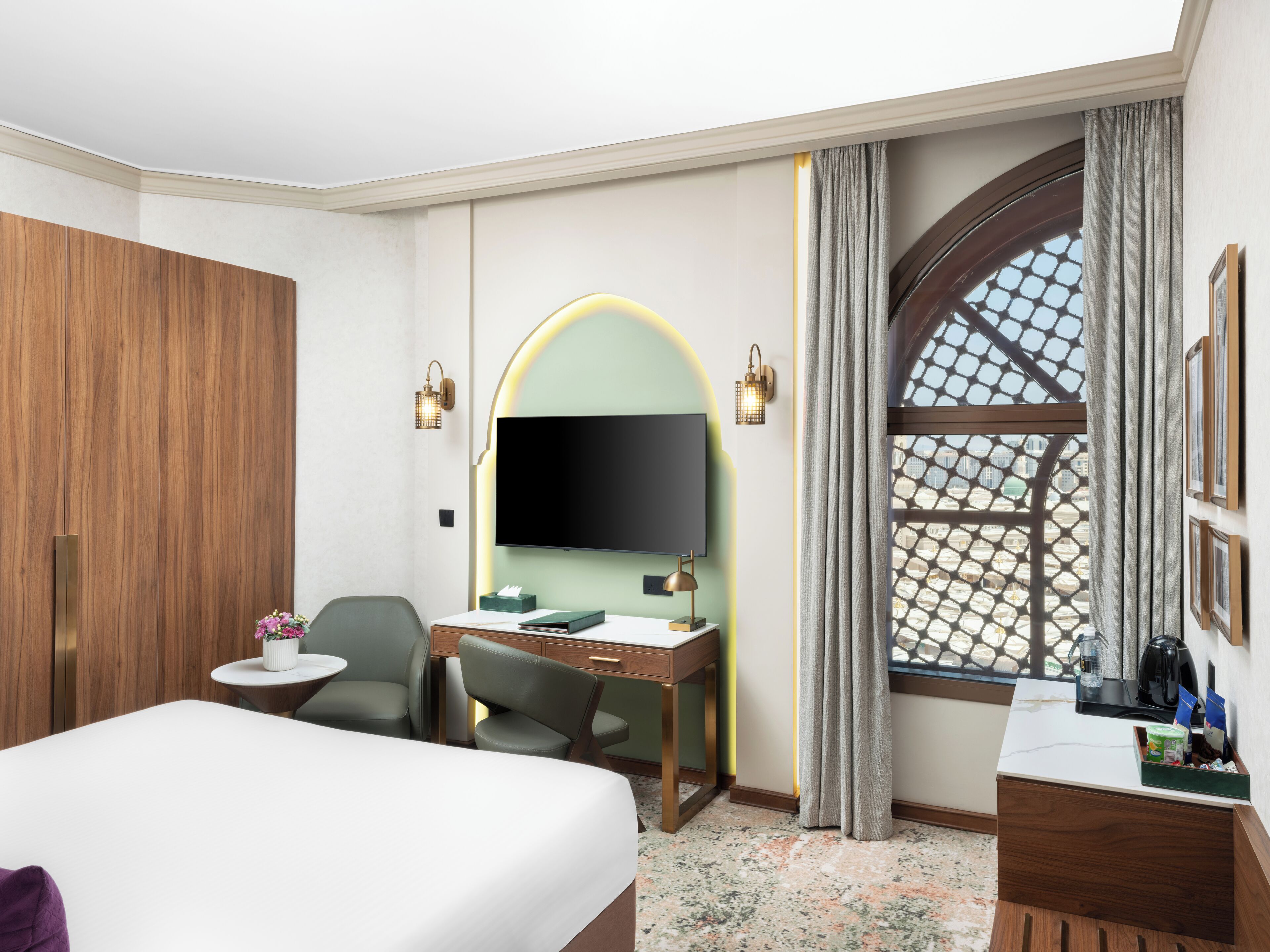 Quarto de hotel com uma cama grande, uma mesa com cadeira, televisão e janela com vista para prédios.