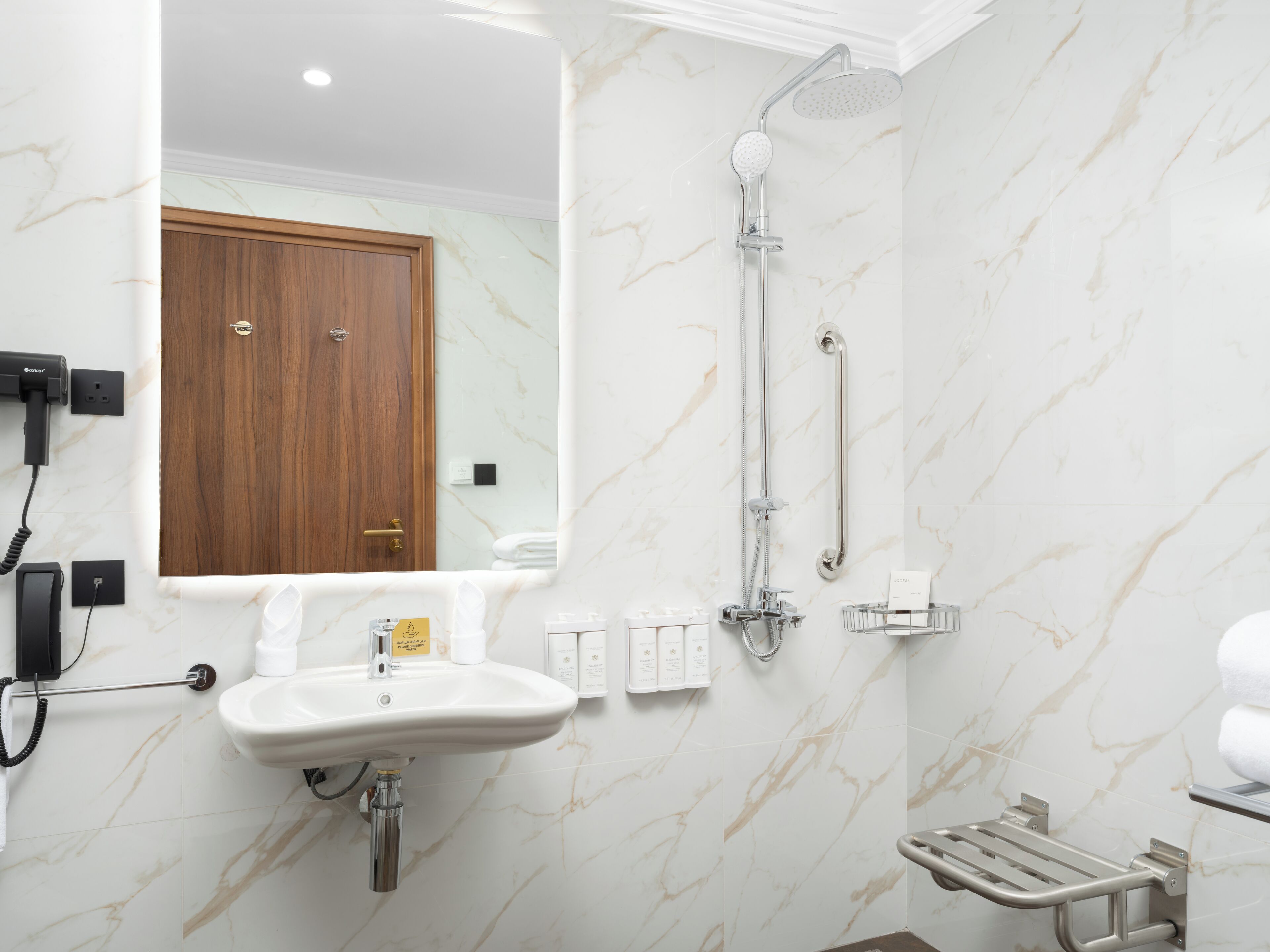 A bathroom with a marble wall, a sink, a mirror, a shower with a handheld showerhead, and a towel rack.