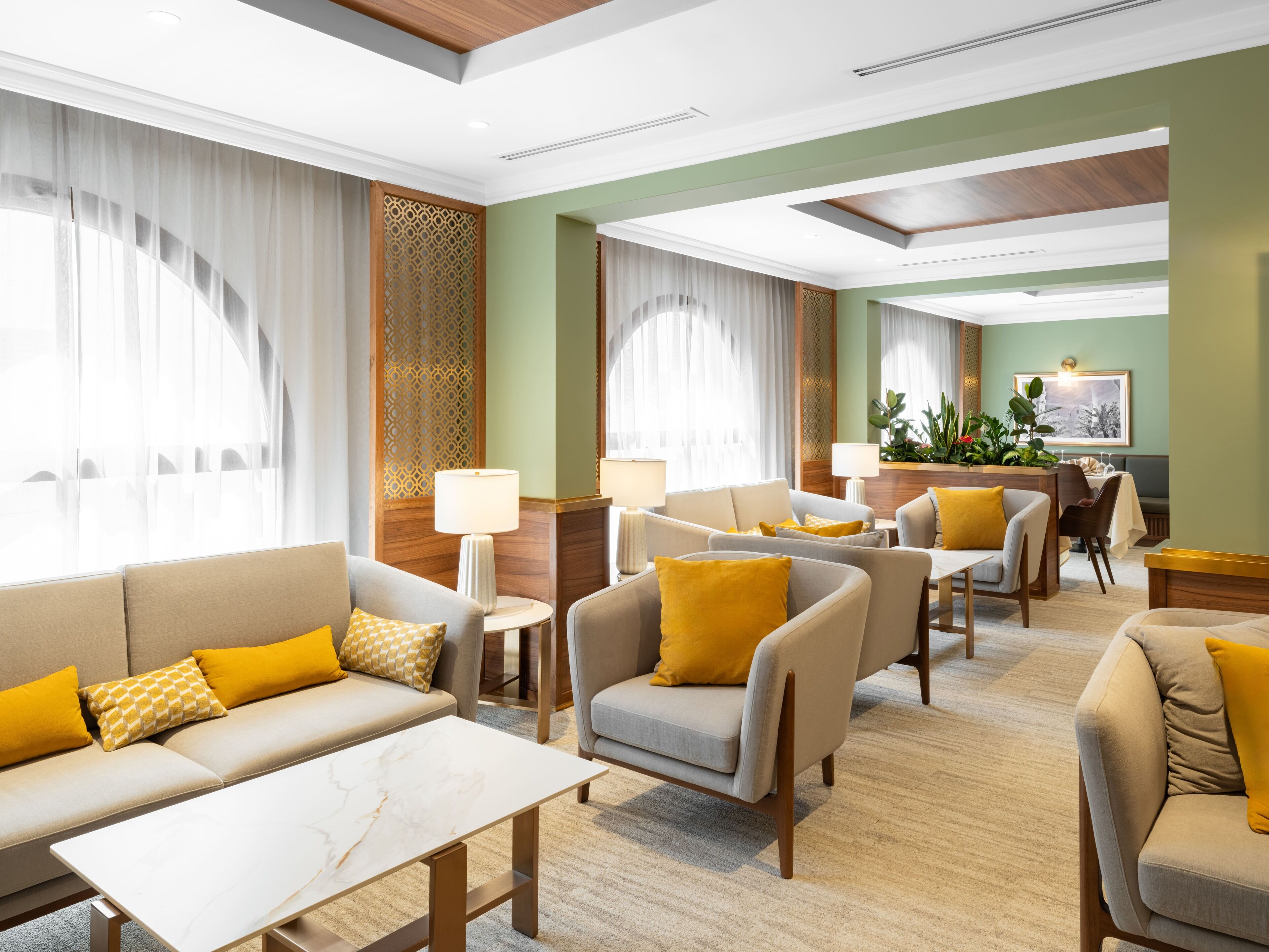 Un hall de hotel con un sofá, sillones y una mesa de centro. Hay lámparas, una planta y un cuadro en la pared.