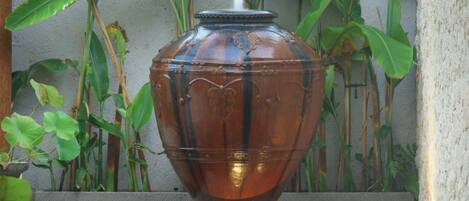 A large, clear glass vase on a wooden platform with a water feature below, surrounded by lush green plants.