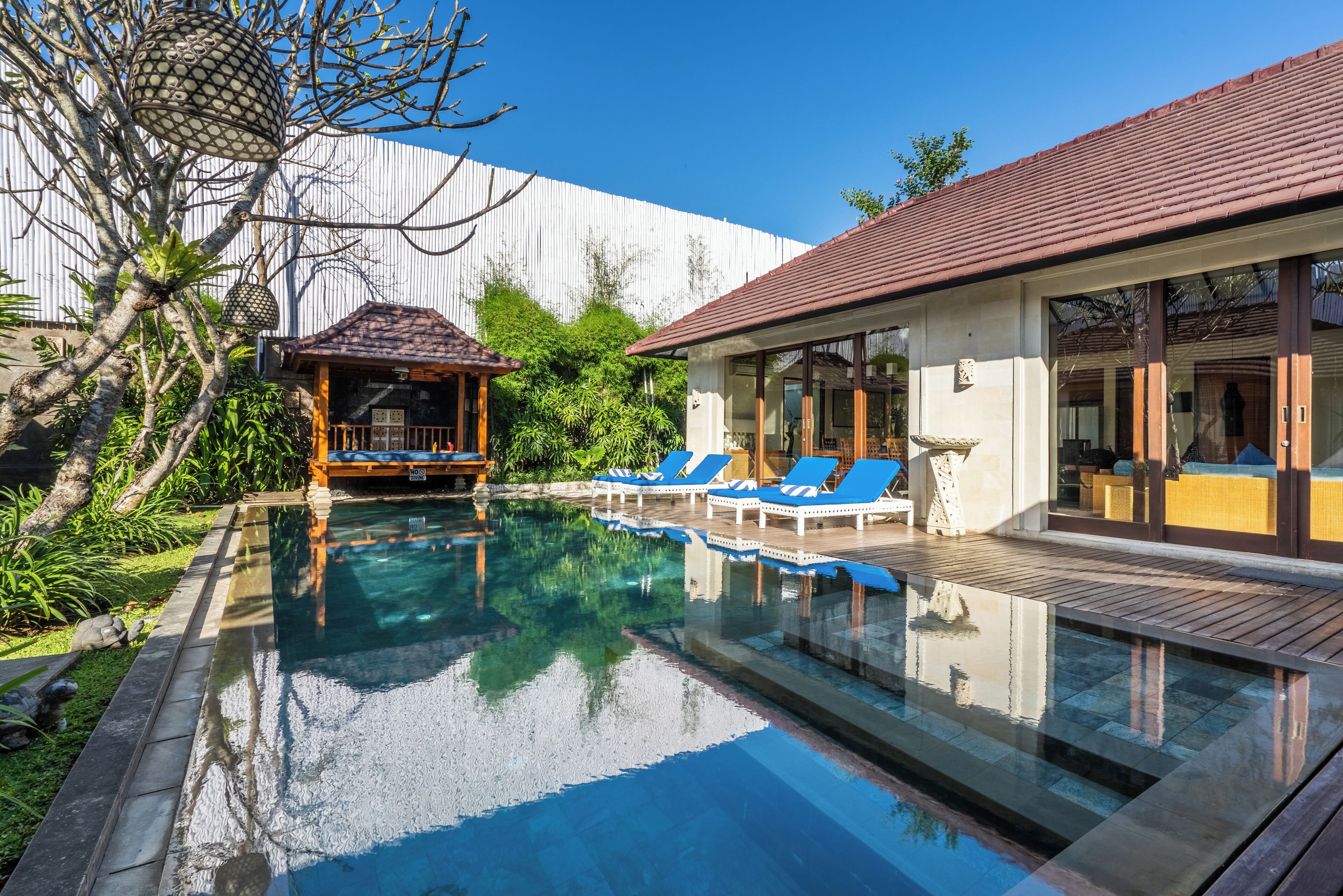 A swimming pool with blue lounge chairs, a wooden deck, and a white building with large windows.