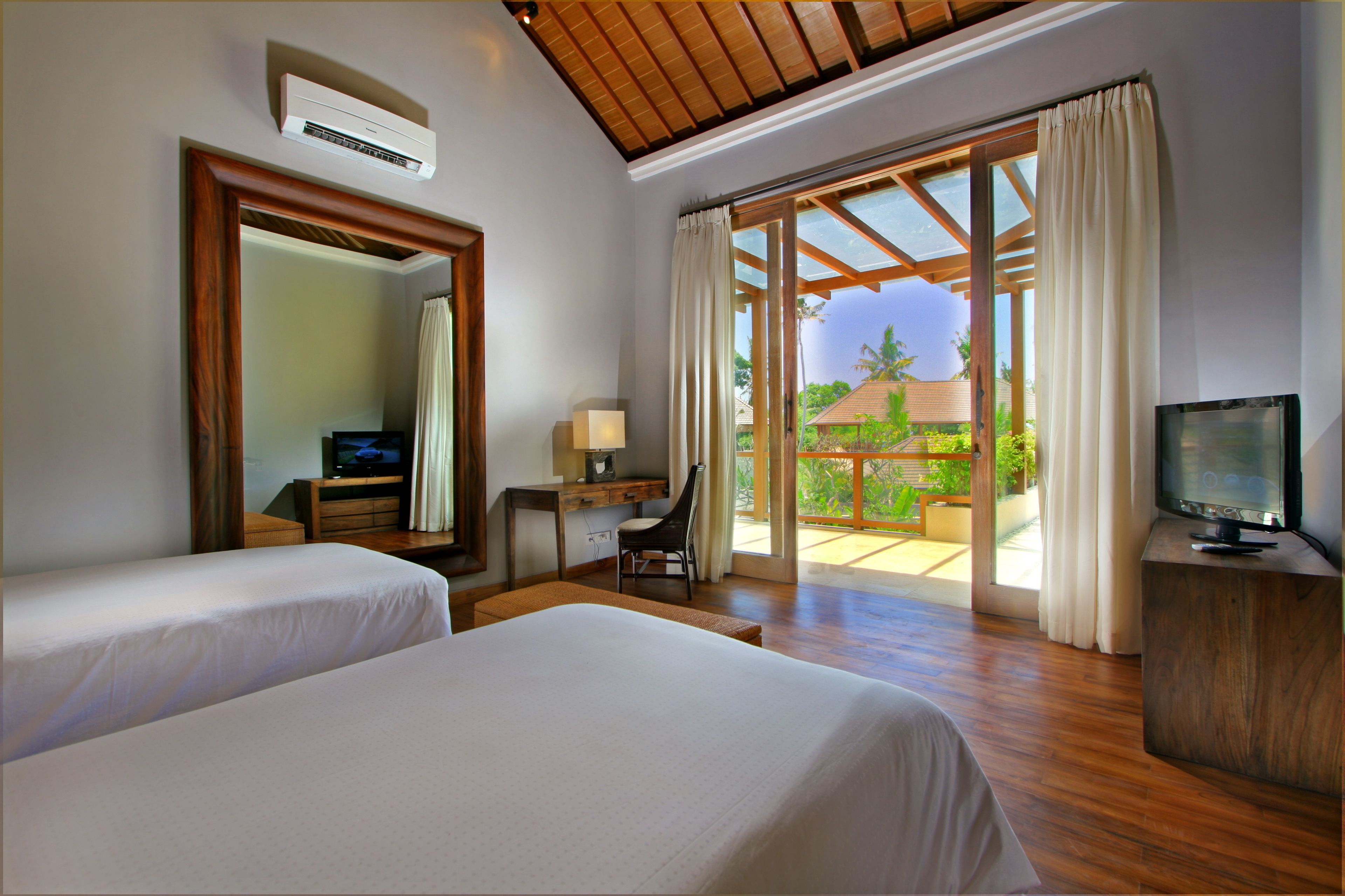 A hotel room with two beds, a desk with a chair, a TV, and a large window with curtains.
