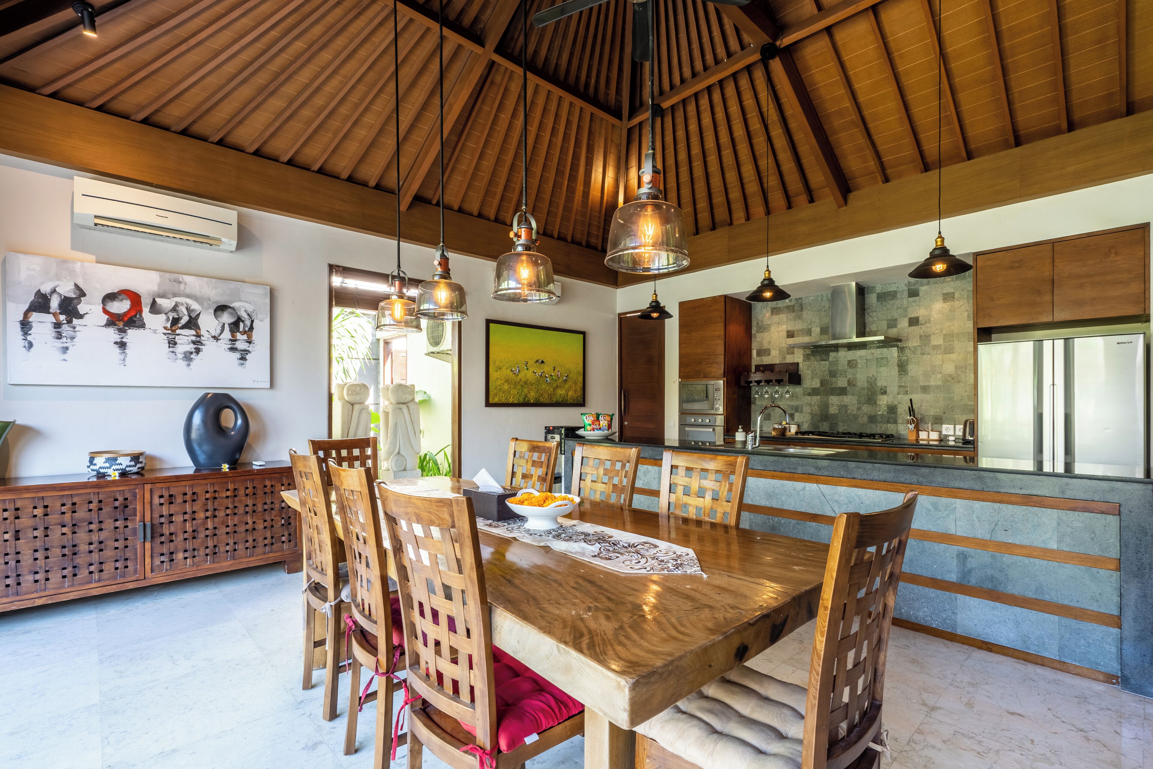 Uma sala de jantar ampla com uma mesa e cadeiras de madeira, uma cozinha ao fundo e obras de arte nas paredes.