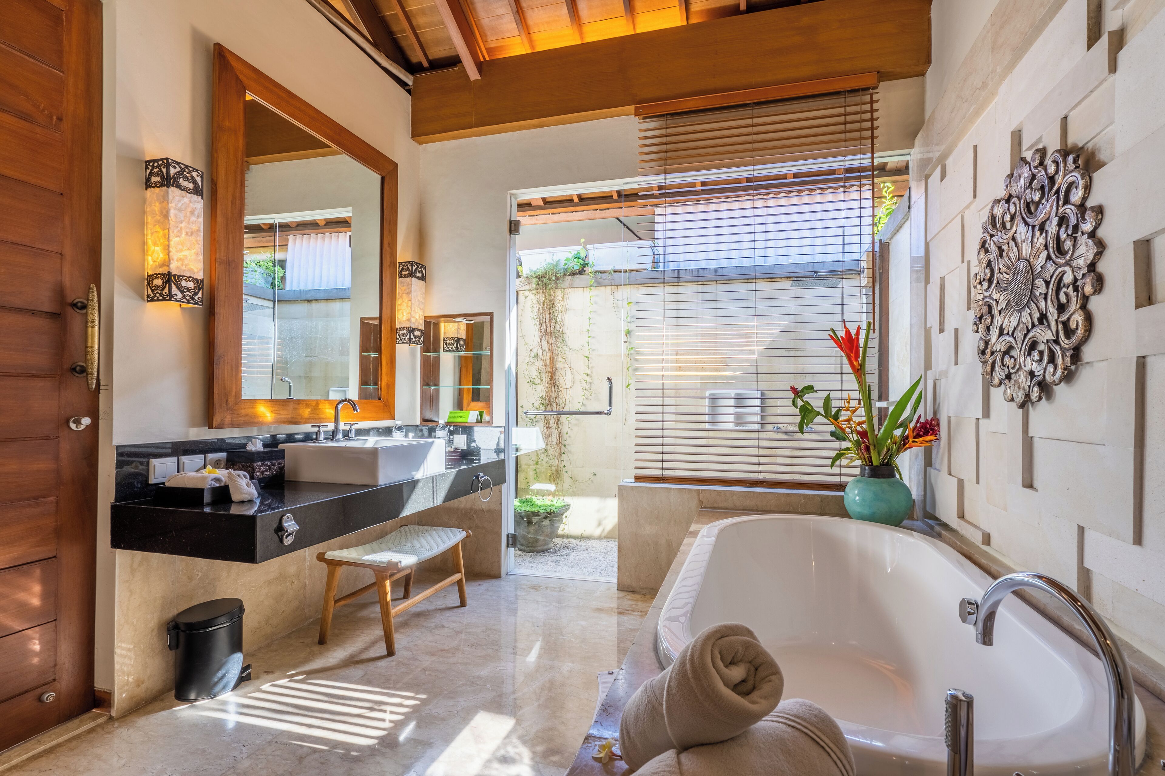 A modern bathroom with a large bathtub, a double sink vanity, and a wooden bench.
