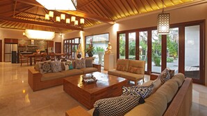 A spacious living area with a large wooden coffee table, two sofas with patterned cushions, and a dining area with wooden furniture. - The Akasha Seminyak Bali Luxury Villas (Seminyak)