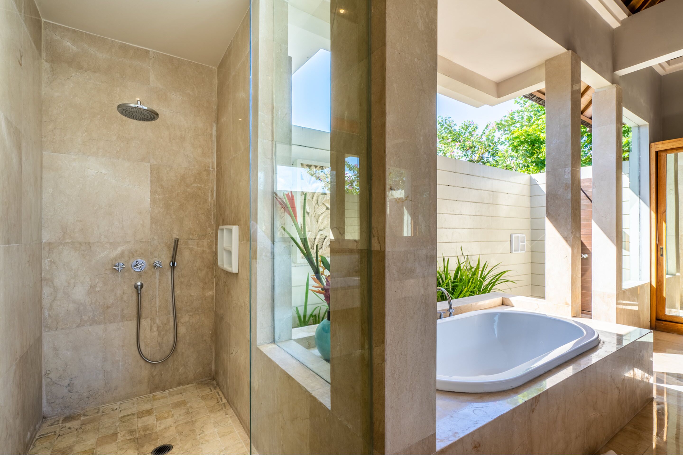 A modern bathroom with a glass-enclosed shower, a freestanding bathtub, and a view of the outdoors.