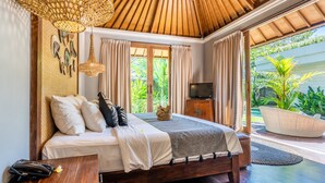 A spacious bedroom with a large bed, a television, and a view of lush greenery outside. - The Akasha Seminyak Bali Luxury Villas (Seminyak)