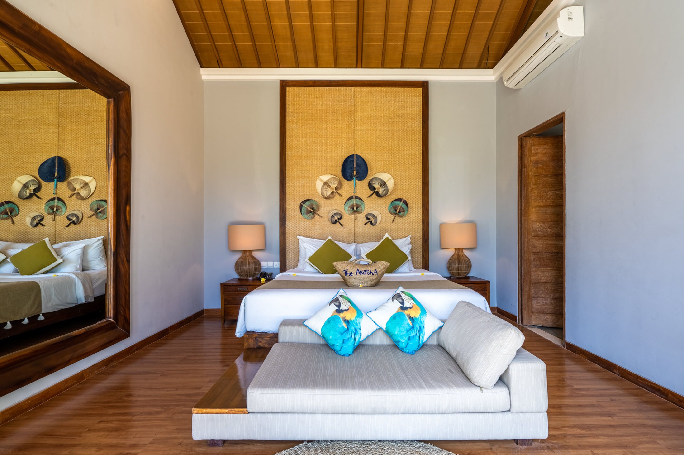 A hotel room with a large bed, a sofa, a mirror, and a decorative wall piece.