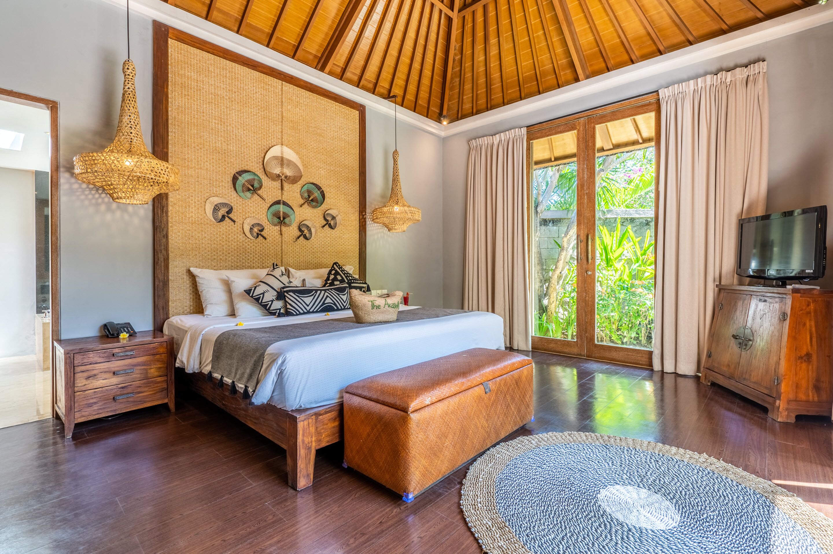 Een slaapkamer met een houten plafond, een groot bed, een houten nachtkastje, een televisie en uitzicht op groen.