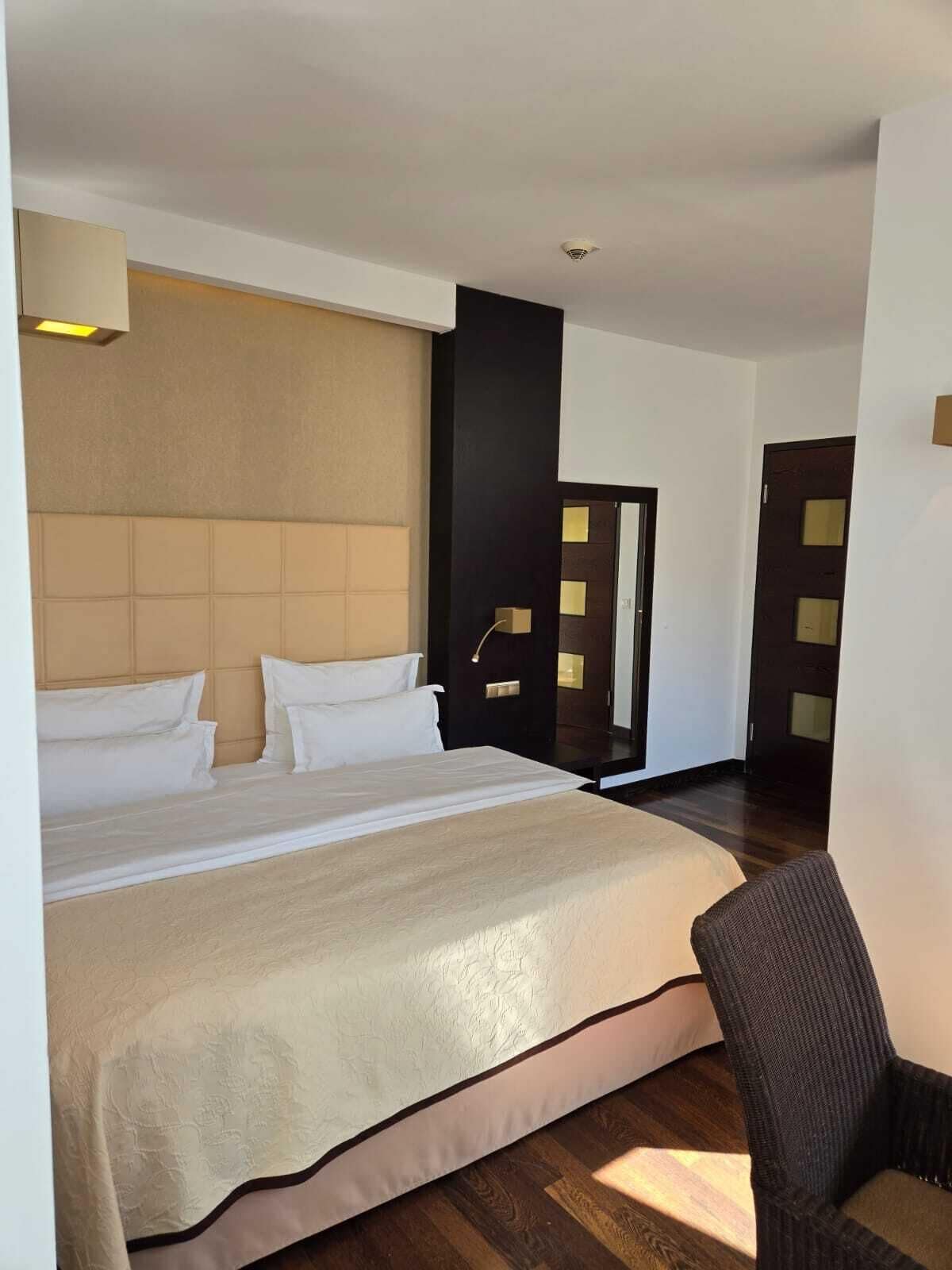 A hotel room with a large bed, a chair, a door with glass panels, and a ceiling light.