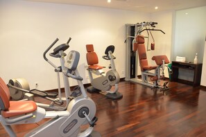 A gym with various exercise machines, including treadmills and weight machines, in a room with wooden flooring and white walls. - MyPlace Premium Apartments (Vienna)