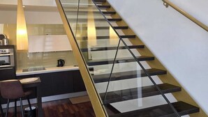 A modern interior with a glass staircase, a kitchen area, and a dining space.