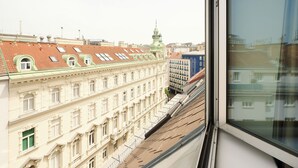 A view of a building with multiple windows and a green spire, seen from a window with a white frame.