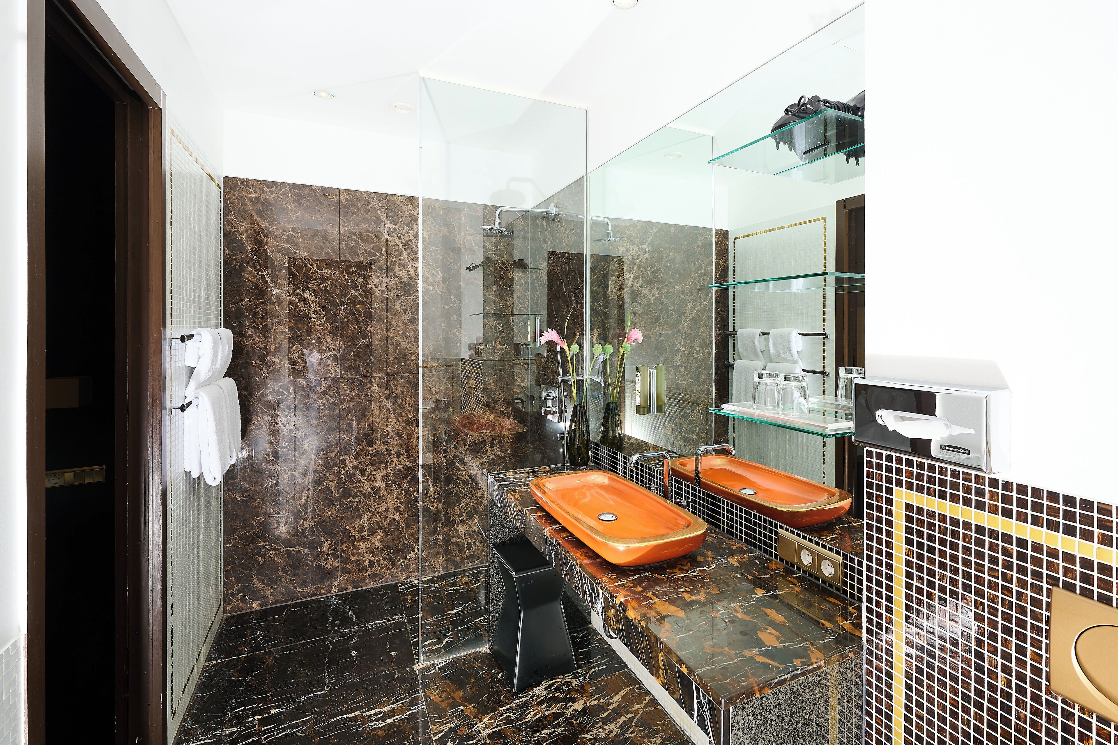 Une salle de bain moderne dotée d’une douche à parois de verre, de deux vasques avec des plans de travail en marbre et d’un grand miroir.