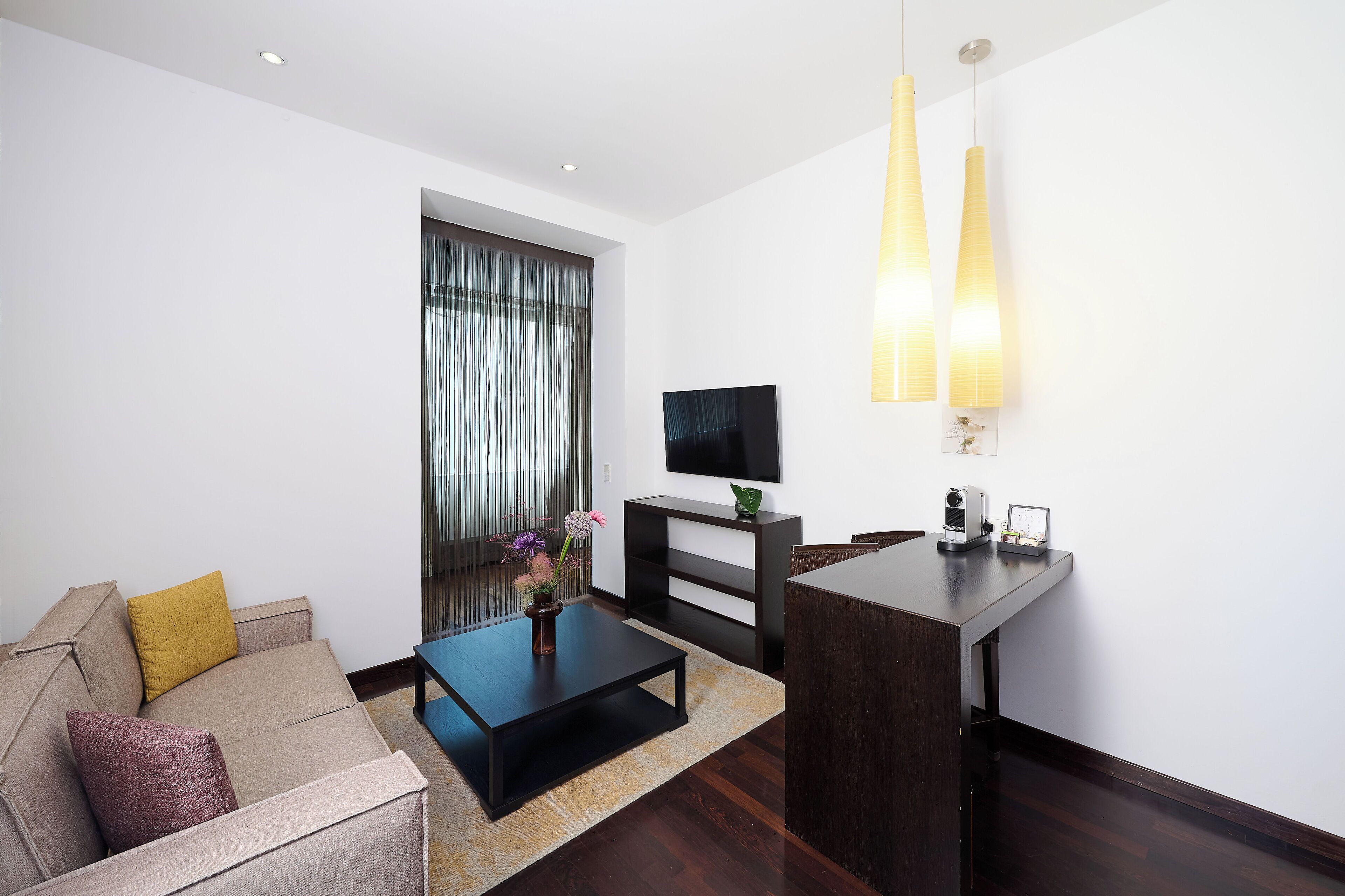 Een moderne woonkamer met een bank, salontafel, televisie en een bureau met een lamp.