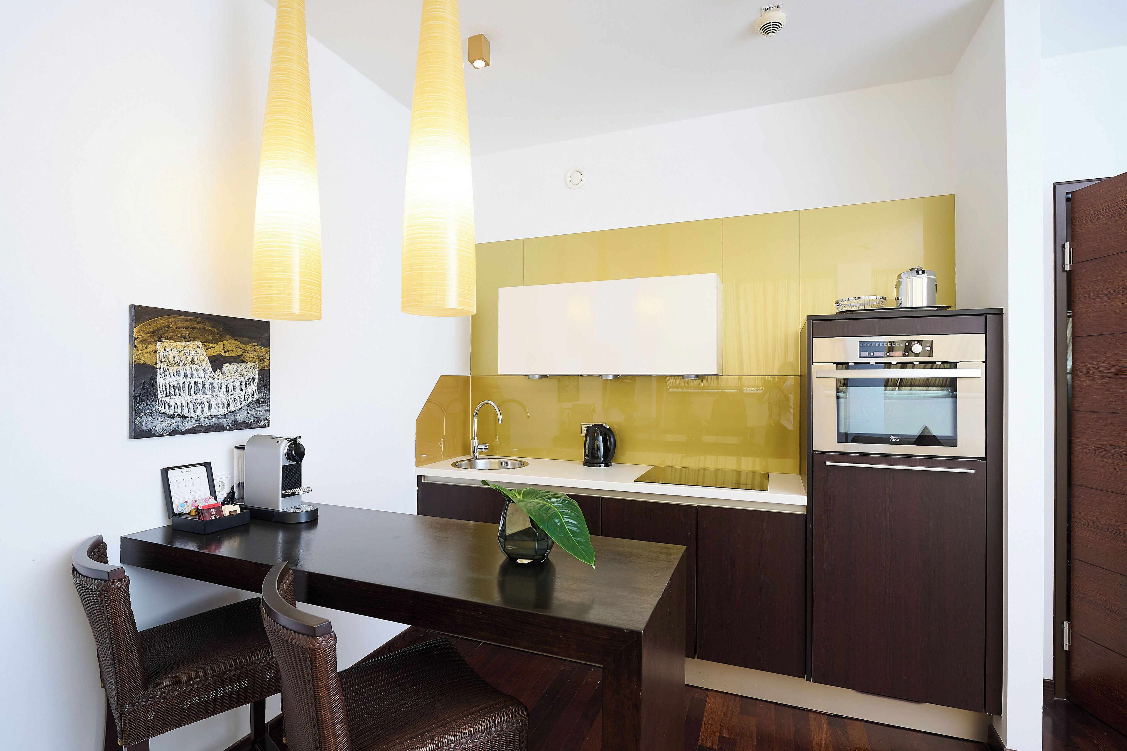 Cocina compacta con comedor, diseño moderno que incluye un salpicadero amarillo, horno empotrado y cafetera.