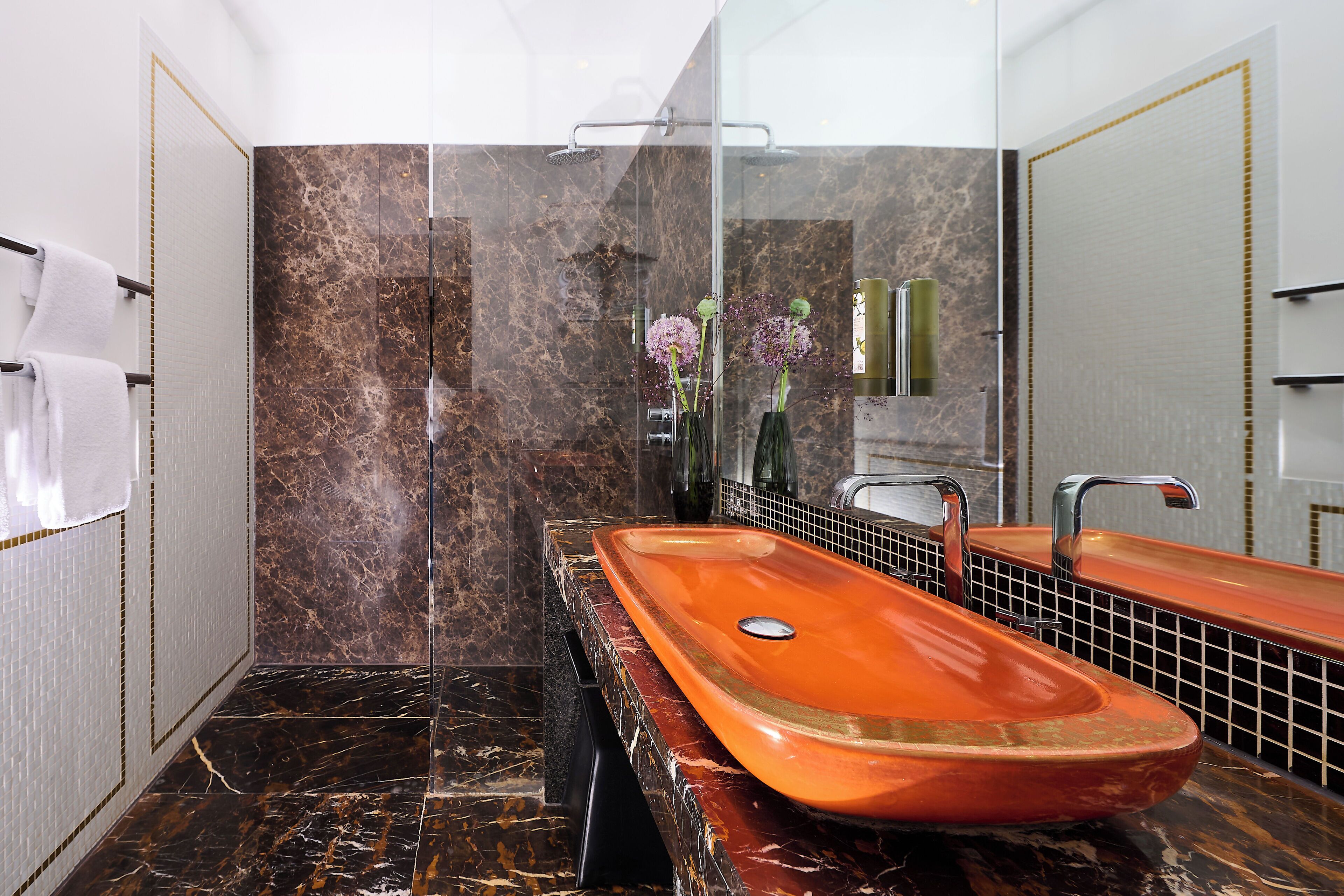 A bathroom with a large oval sink, a glass shower enclosure, and a mirror with a gold frame.