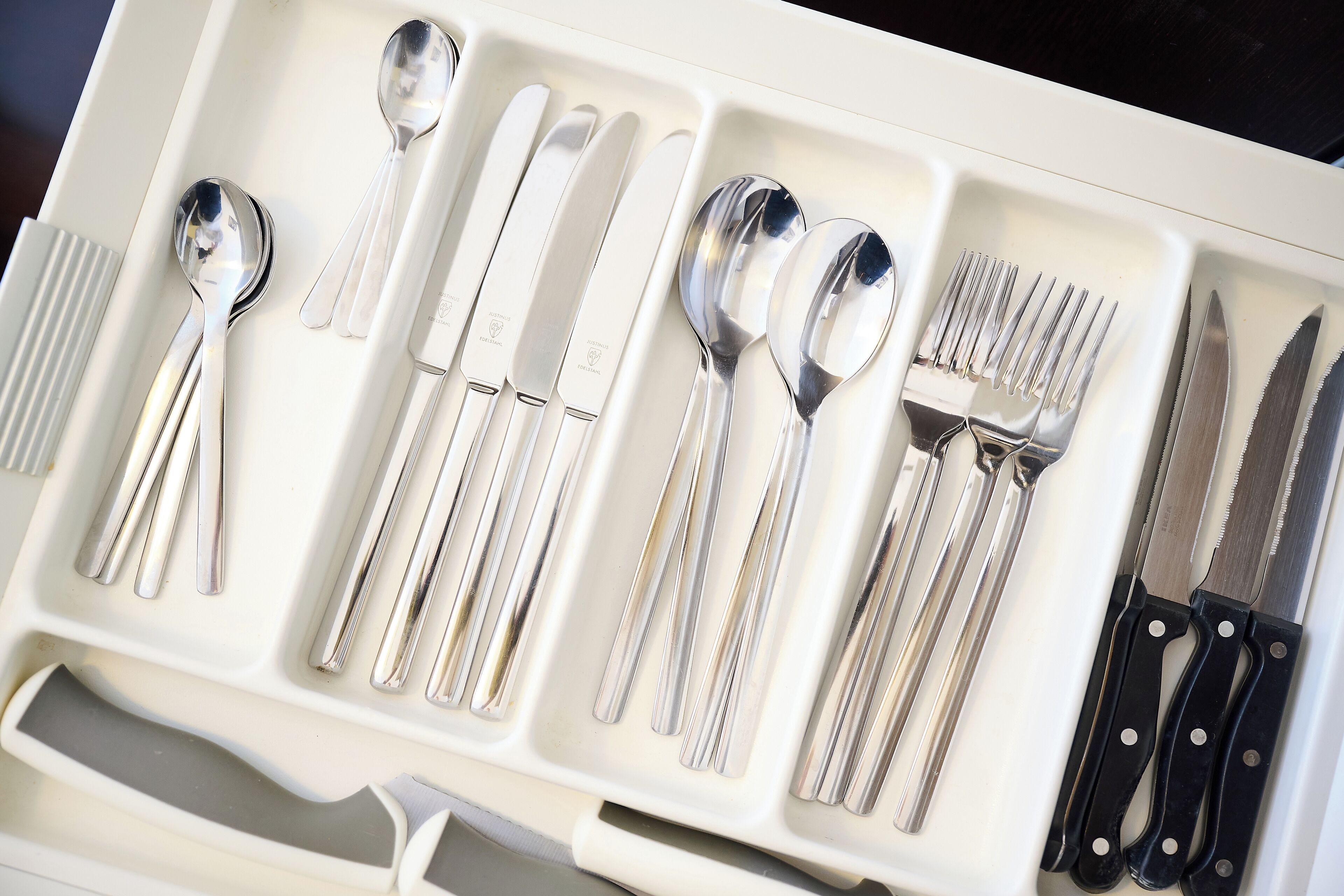 A drawer containing various silverware including spoons, forks, knives, and a spoon rest.