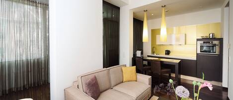 Una sala de estar moderna con un sofá, una mesa de centro con jarrones, y una zona de cocina con una mesa de comedor y sillas.
