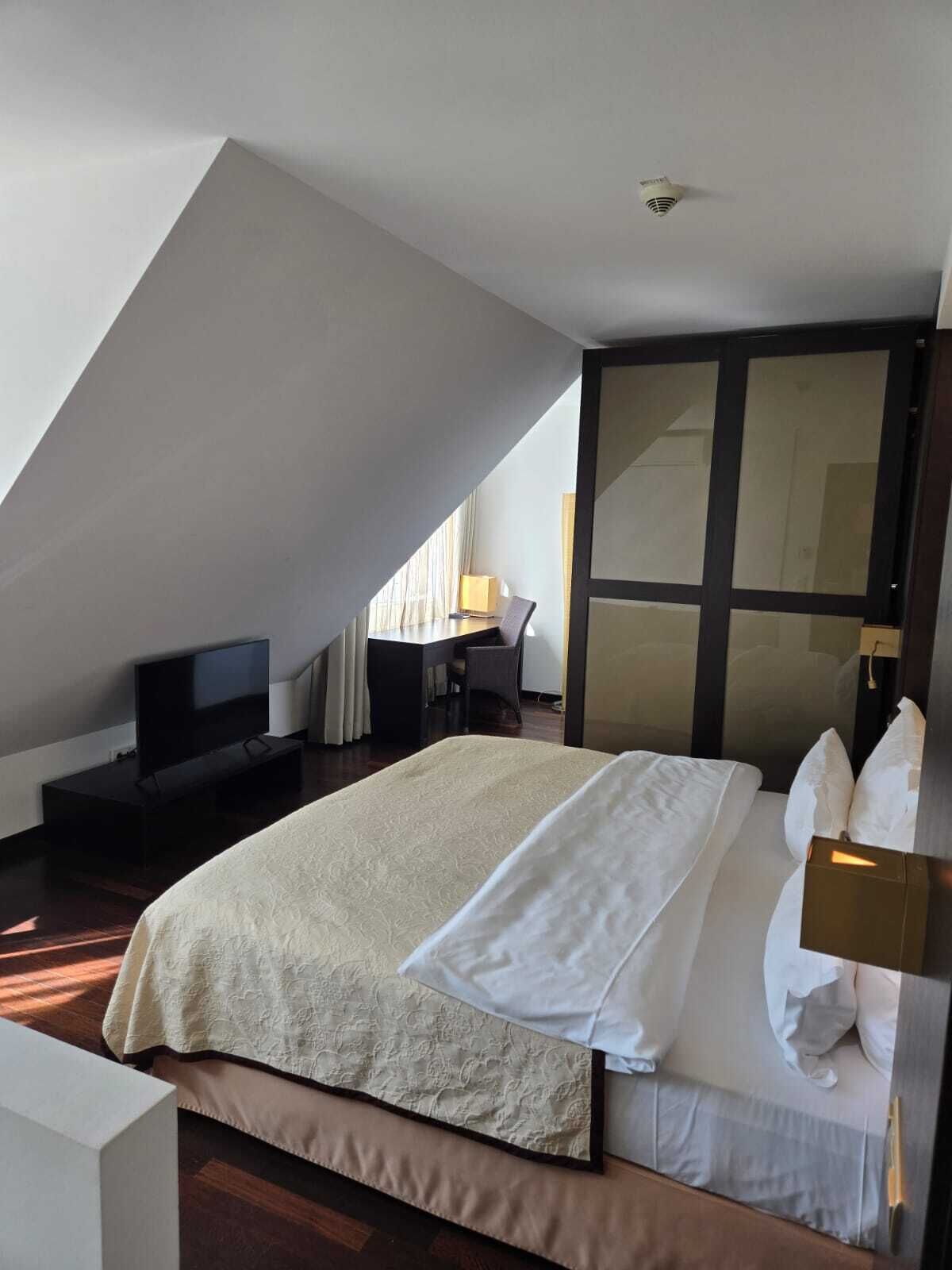 A modern hotel room with a large bed, a desk, a television, and a sliding door.