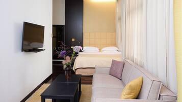 Una habitación de hotel con cama, sofá, televisión montada en la pared y una mesita con un jarrón de flores.