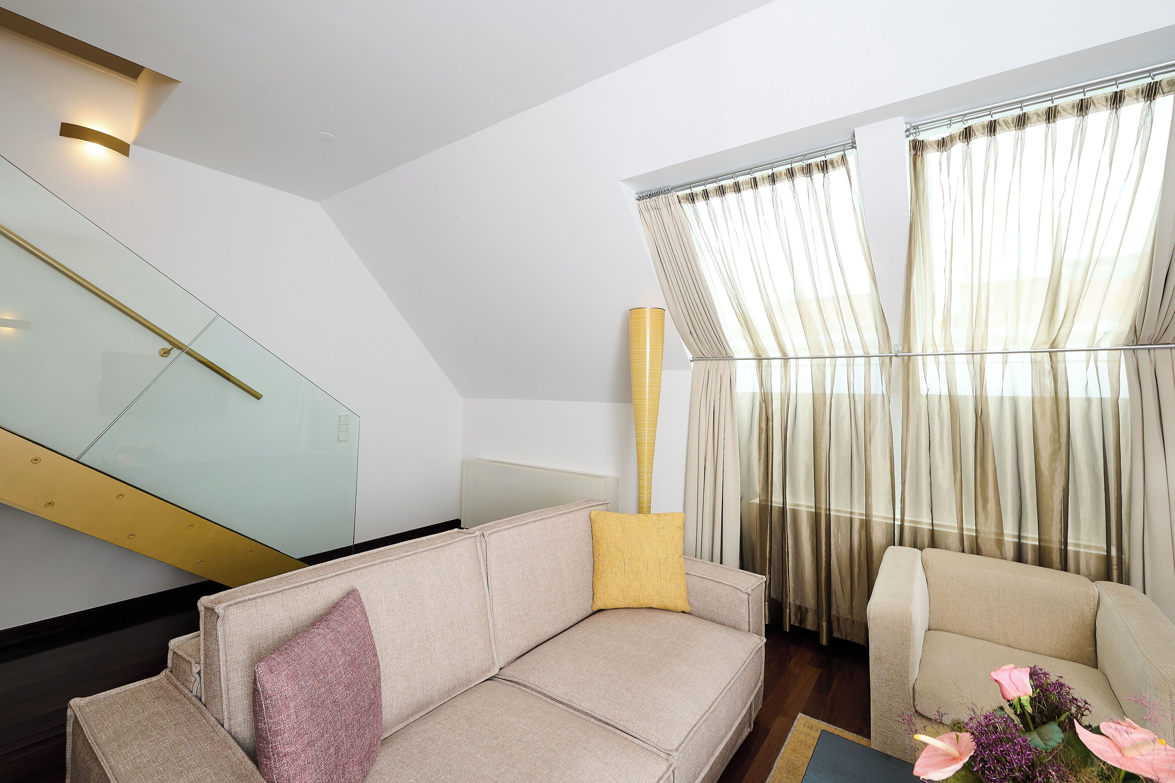 A modern living room with a beige sofa, a yellow accent pillow, and a small table with flowers.