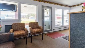 A reception area with two armchairs, a small table, a red mat, and a counter with a TV above it. - Best Travel Inn Philipsburg (Philipsburg)