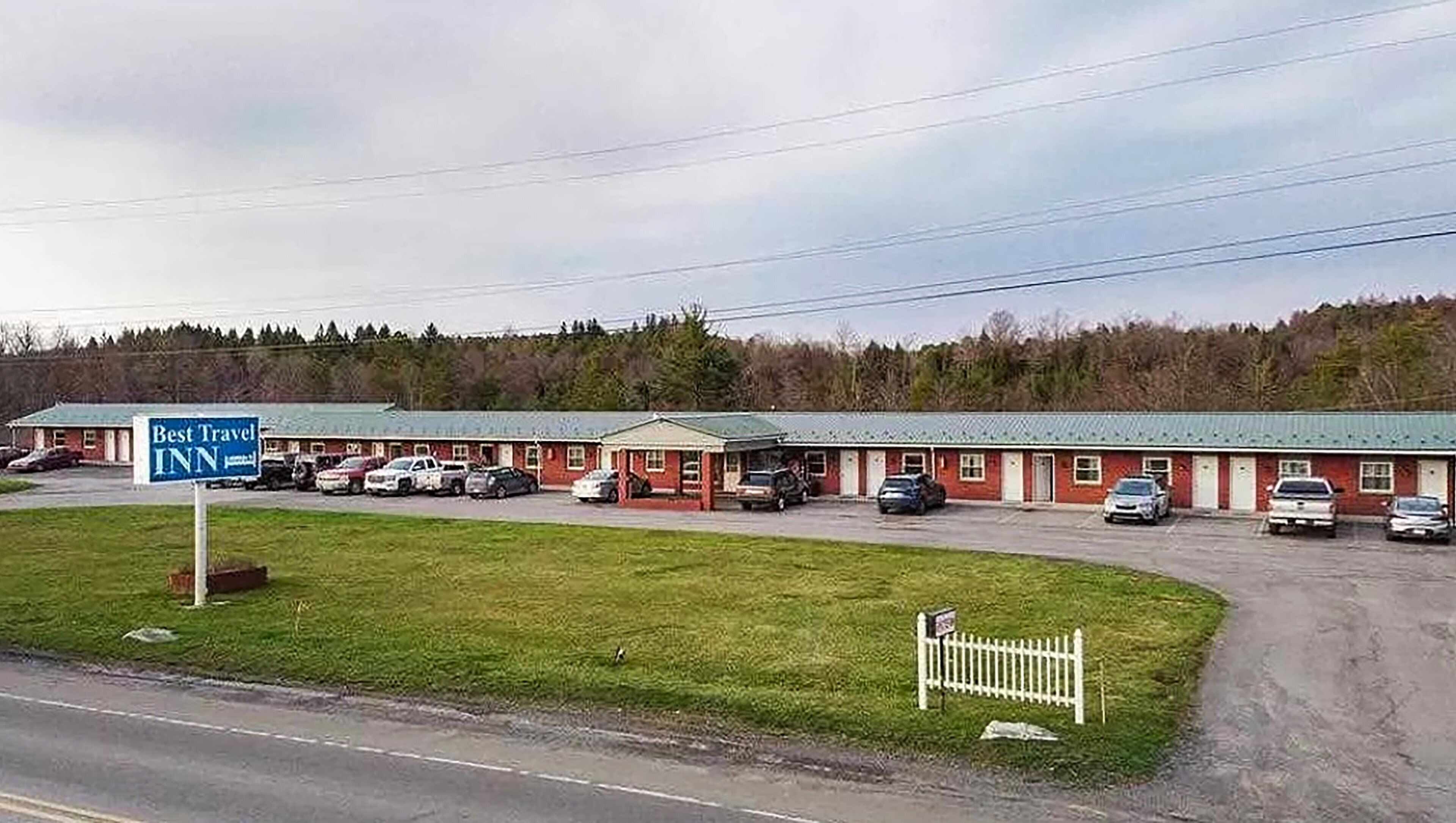 A Best Travel Inn with a row of single-story buildings, a parking lot, and a grassy area in front.