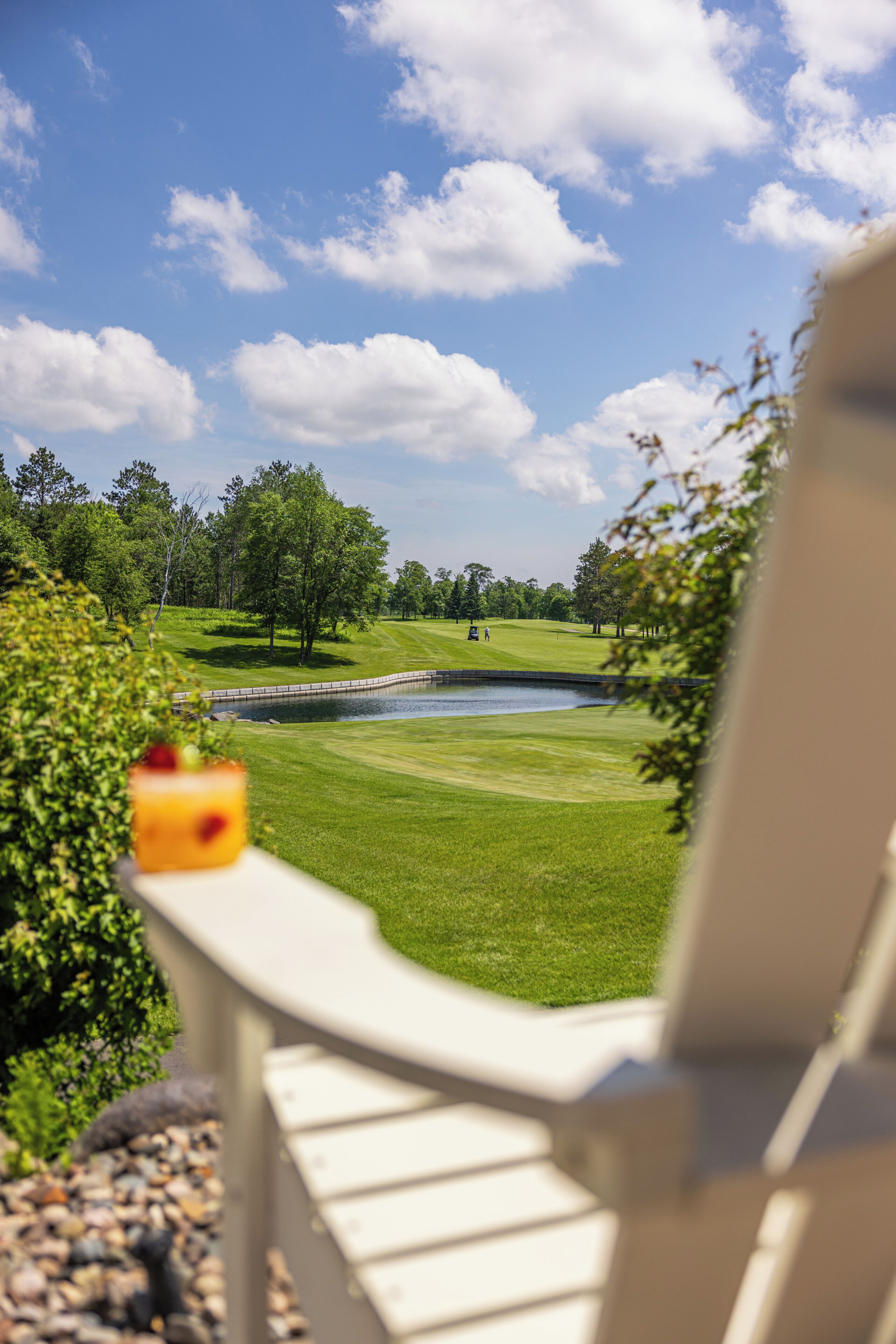 A view of a golf course with a pond, trees, and a clear sky.