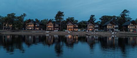 A row of wooden cabins by a calm lake at dusk.