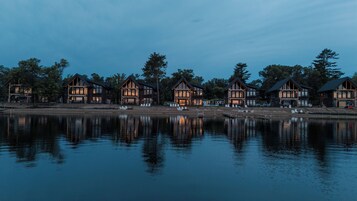 A row of wooden cabins by a calm lake at dusk.