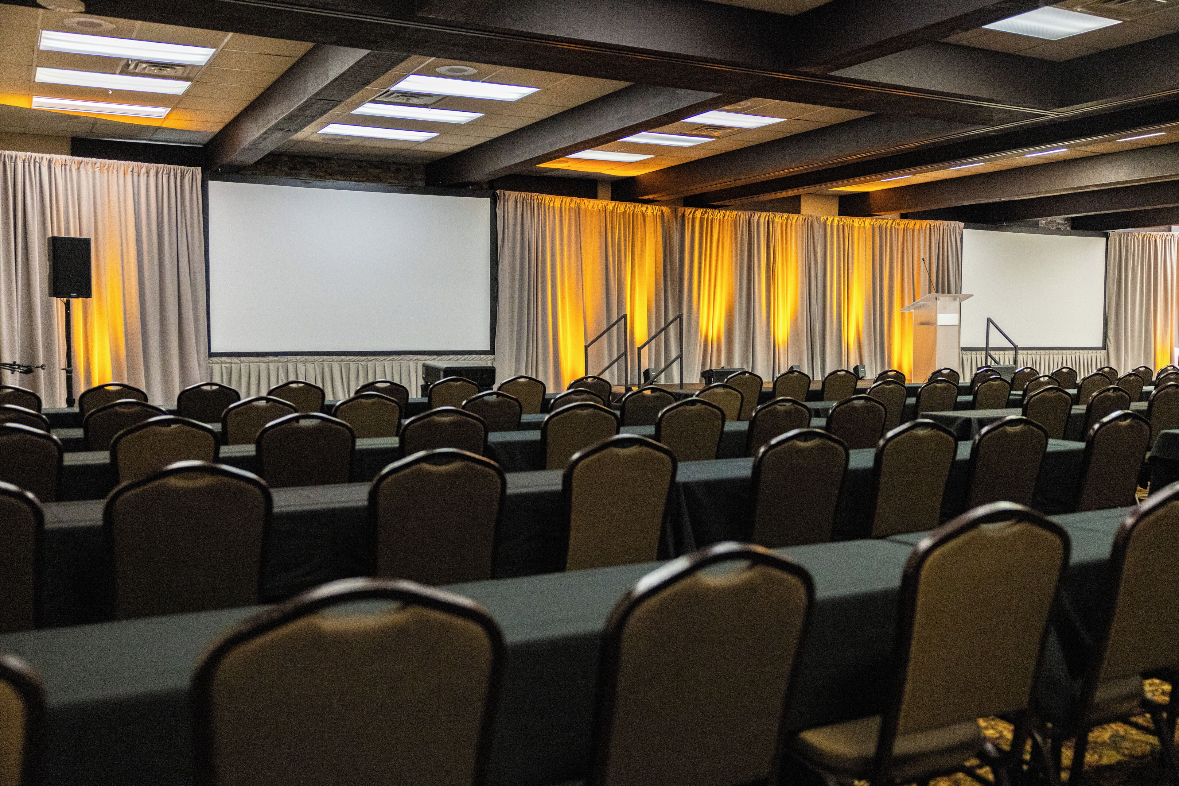 Un salón de conferencias con filas de sillas, un atril y una pantalla de proyección.